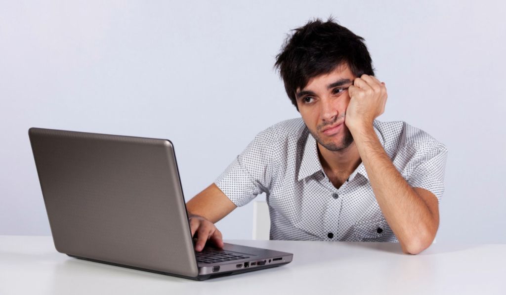 homme assis à son bureau devant son ordinateur. Il se tient la tête l'air dépité devant son site wordpress qu'il ne comprend pas